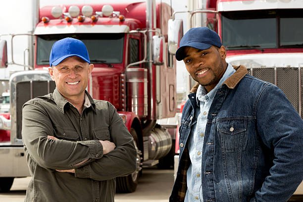 Two Smiling Truck Drivers Standing in Front of Their Trucks.